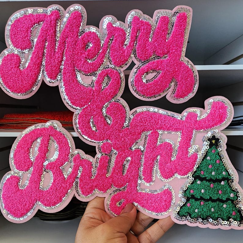 Peut inclure: Un &eacute;cusson rose textur&eacute; avec les mots "Merry & Bright" en &eacute;criture cursive, bord&eacute; de paillettes argent&eacute;es. Un sapin de No&euml;l vert avec des ornements roses et une &eacute;toile est &agrave; droite. Parfait pour les cr&eacute;ations de No&euml;l.