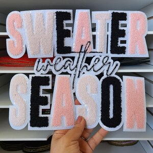 Peut inclure: Patch "Sweater Weather Season" aux lettres roses, noires et cr&egrave;me, &agrave; texture duveteuse. Les lettres sont bord&eacute;es de paillettes. Id&eacute;al pour la d&eacute;coration de v&ecirc;tements ou d'accessoires.