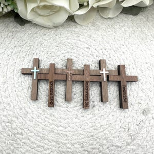May include: Five wooden crosses with varying designs and text. Each cross is a dark brown color, with a light blue, white, and gold cross design. The text includes Bible verses: Ephesians 2:8-10, Deuteronomy 5:6, and Psalm 23:4.
