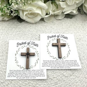 May include: Two wooden crosses on cards with the text "Pocket of Faith". The crosses are dark brown with a smaller cross in the center. The cards have a floral wreath design and inspirational text.