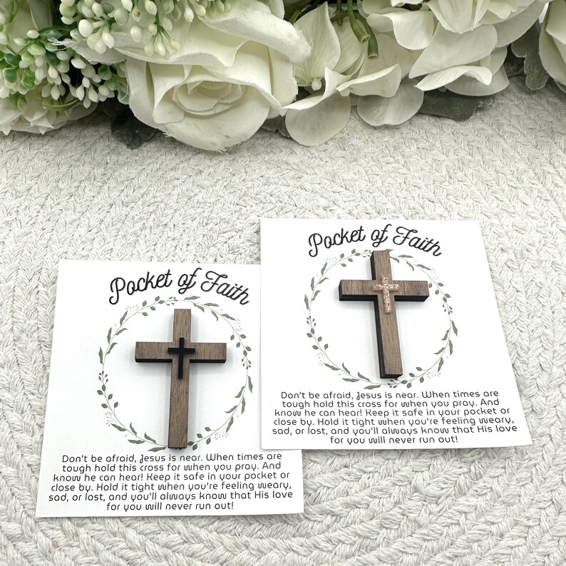 May include: Two wooden crosses on cards with the text "Pocket of Faith". The crosses are dark brown with a smaller cross in the center. The cards have a floral wreath design and inspirational text.