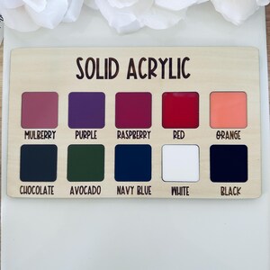 May include: A wooden color chart labeled "SOLID ACRYLIC" with ten color swatches: Mulberry, Purple, Raspberry, Red, Orange, Chocolate, Avocado, Navy Blue, White, and Black. The colors are displayed in square shapes.