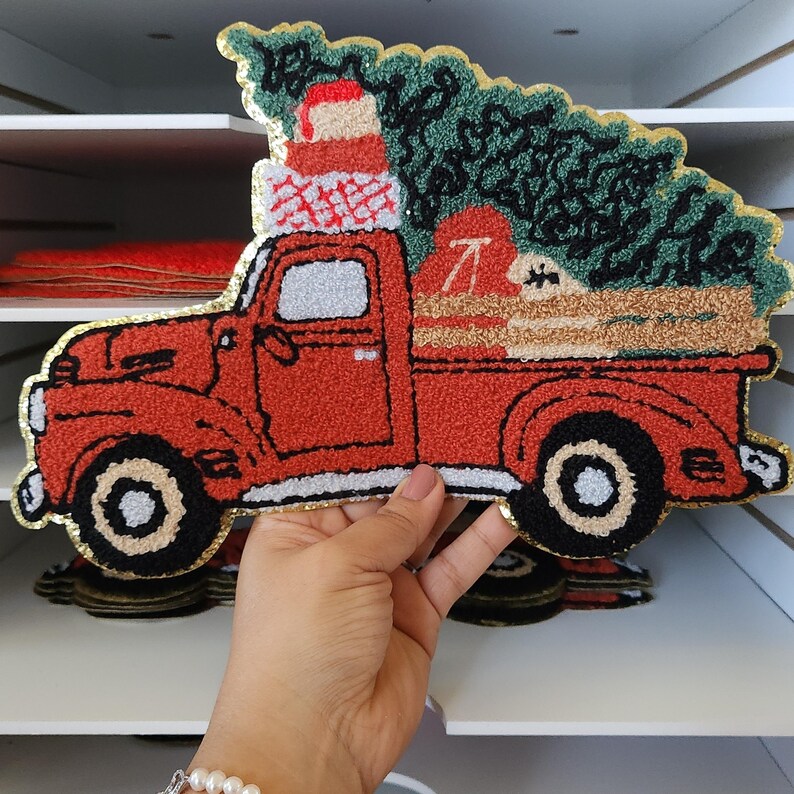 Peut inclure: Un camion rouge vintage transportant un sapin de No&euml;l et des cadeaux emball&eacute;s. Le camion a des pneus noirs avec des accents blancs et dor&eacute;s. L'arbre est vert et les cadeaux sont rouges et blancs. L'image a un aspect brod&eacute; textur&eacute;.