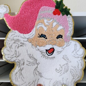 Peut inclure: D&eacute;coration de visage de P&egrave;re No&euml;l avec un bonnet rose, une barbe blanche et une bordure dor&eacute;e scintillante. Le P&egrave;re No&euml;l a les yeux bleus, une bouche rouge et un teint clair. Le design est fait d'un mat&eacute;riau textur&eacute;, parfait pour les f&ecirc;tes.