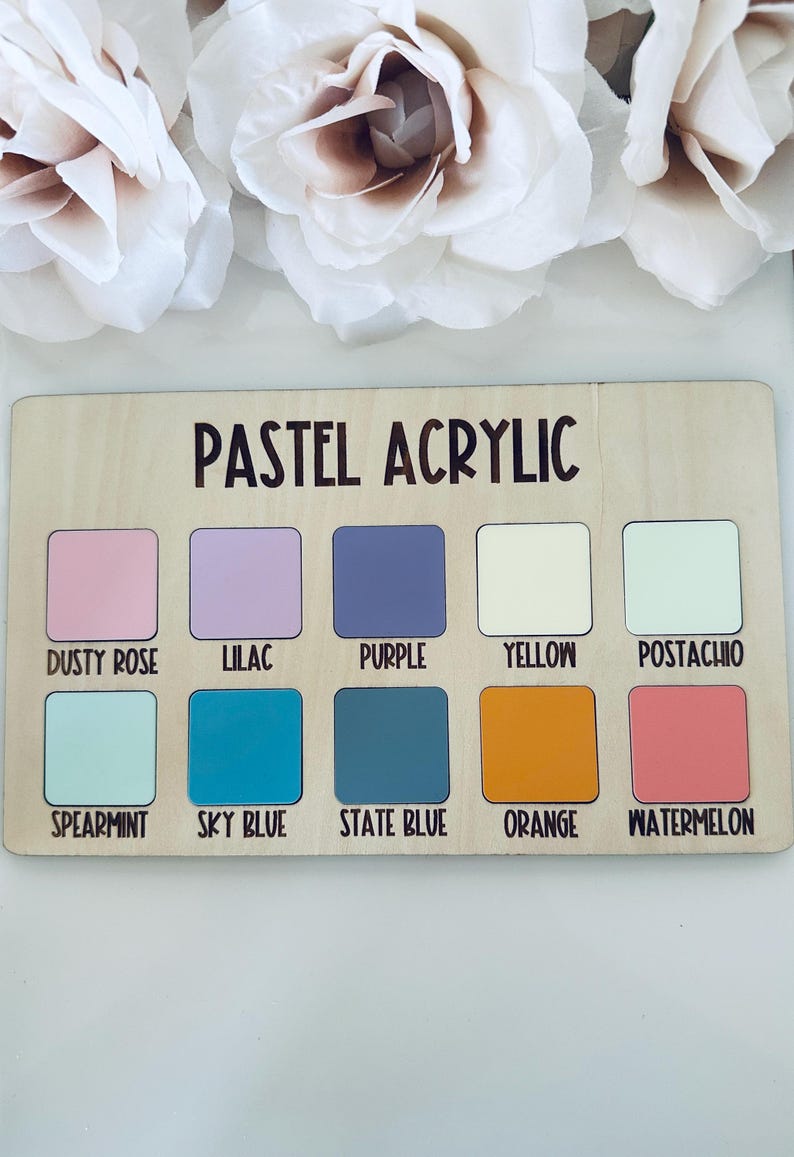 May include: A wooden color palette with the text "PASTEL ACRYLIC" and ten color swatches. Colors include dusty rose, lilac, purple, yellow, pistachio, spearmint, sky blue, state blue, orange, and watermelon. White flowers are in the background.