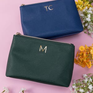 May include: Two zippered pouches with gold lettering. The pouch on top is blue with the letters "TC" on it. The pouch on the bottom is green with the letter "M" on it.