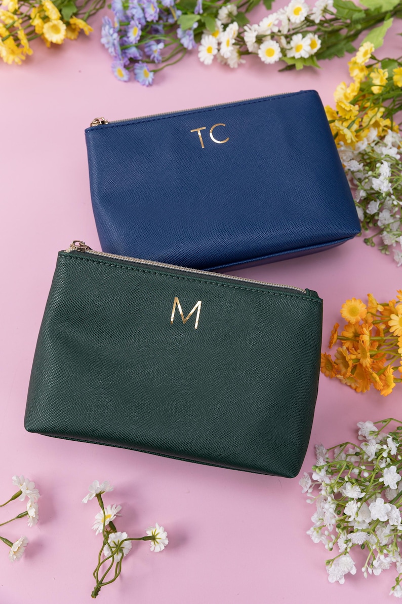 May include: Two zippered pouches with gold lettering. The pouch on top is blue with the letters "TC" on it. The pouch on the bottom is green with the letter "M" on it.