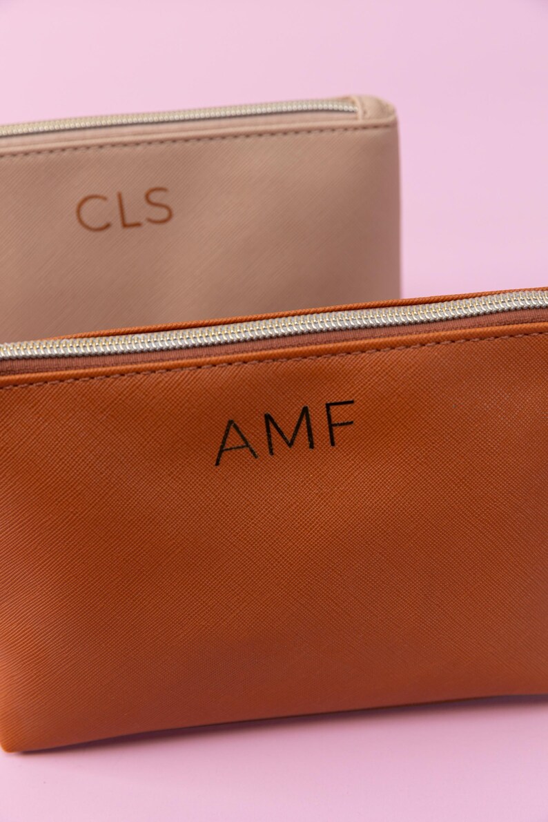 May include: Two zippered pouches, one brown and one beige, with personalized initials. The brown pouch has the initials "AMF" and the beige pouch has the initials "CLS".