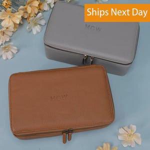 May include: Two rectangular zippered travel cases with a textured finish, one in light gray and one in tan. Each case features the embossed letters MCW on the top lid and includes dual metal zipper pulls for closure, providing a secure storage solution.