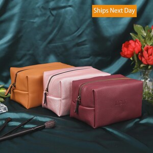 May include: Three rectangular cosmetic bags with a textured finish, featuring a zipper closure. The bags are colored in mustard yellow, light pink, and deep burgundy. The burgundy bag has the letters MCW embossed on the front surface.