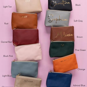 May include: Ten different colored zippered pouches with gold lettering. The pouches are arranged in two rows of five. The colors are light tan, rust, garnet red, blush pink, light blue, champagne, black, soft grey, brown, pine green, orange, and admiral blue.