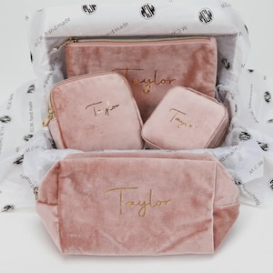 May include: A set of four dusty pink velvet pouches and cases with gold zippers, each featuring the name Taylor in gold script. The items are arranged on white tissue paper printed with the text M.C.W. hand made and a circular logo.