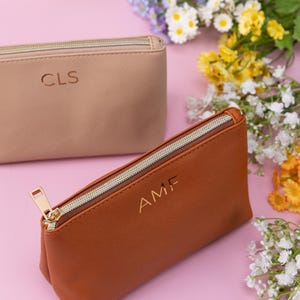 May include: Two zippered pouches with personalized initials. The pouch on the left is beige with the initials "CLS" and the pouch on the right is brown with the initials "AMF".