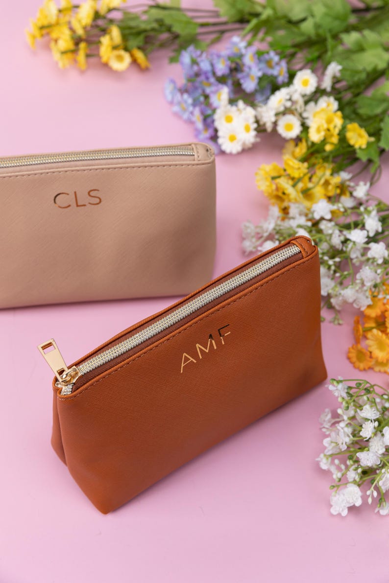 May include: Two zippered pouches with personalized initials. The pouch on the left is beige with the initials "CLS" and the pouch on the right is brown with the initials "AMF".