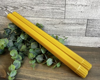 May include: Two long, yellow beeswax candles with wicks. The candles are hexagonal in shape and have a textured surface.