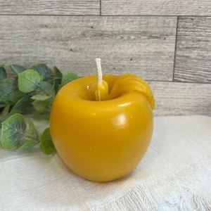May include: A yellow beeswax candle shaped like an apple with a white wick.