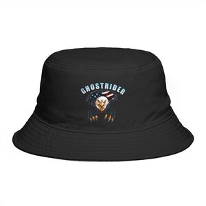 May include: A black bucket hat featuring a graphic print on the front. The design displays a bald eagle with an American flag pattern on its head, sharp talons, and the word GHOSTRIDER printed in light blue capital letters above the eagle.