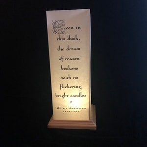 May include: A white paper lantern with a black inscription that reads "Even in this dusk, the dream of reason beckons with its flickering bright candles." The lantern is on a wooden base with the inscription "Philip Appleman 1926-2020".