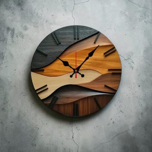 May include: A round wooden wall clock with a layered design. The clock face features a wave-like pattern in shades of black, brown, tan, and orange. Black hands and hour markers complete the design. The clock measures approximately 12 inches in diameter.