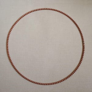 May include: A circular hoop constructed from a single continuous length of twisted copper wire. The metal has a warm, reddish-brown metallic finish with a repeating spiral texture along the entire circumference of the ring-shaped object.