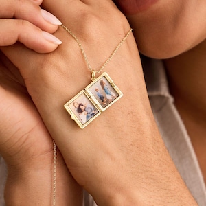 Puede incluir: Un collar con un medallón dorado con dos compartimentos rectangulares, cada uno con una pequeña fotografía. El medallón está abierto, revelando las fotos. El collar se sostiene en la mano de una persona.
