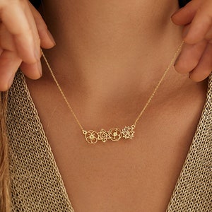 Könnte beinhalten: Eine goldene Halskette mit einer zarten Kette und einem Anhänger mit einer Reihe von vier ausgeschnittenen Blumenmotiven.