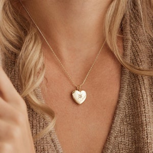 May include: A gold heart-shaped locket necklace with a small diamond-like stone in the centre. The locket is on a delicate gold chain.