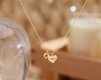 May include: A gold-toned chain necklace featuring two small heart-shaped pendants. One pendant is engraved with the name Sophia, while the other smaller heart pendant displays a tiny red circular stone at its center, suspended from the delicate chain.