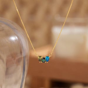 May include: A gold chain necklace with a pendant featuring three teardrop-shaped gemstones in shades of green and blue.