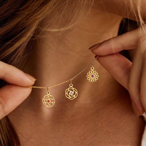 May include: Gold necklace with three flower charms. Each charm has a small gemstone in the center. The gemstones are red, purple, and pink.