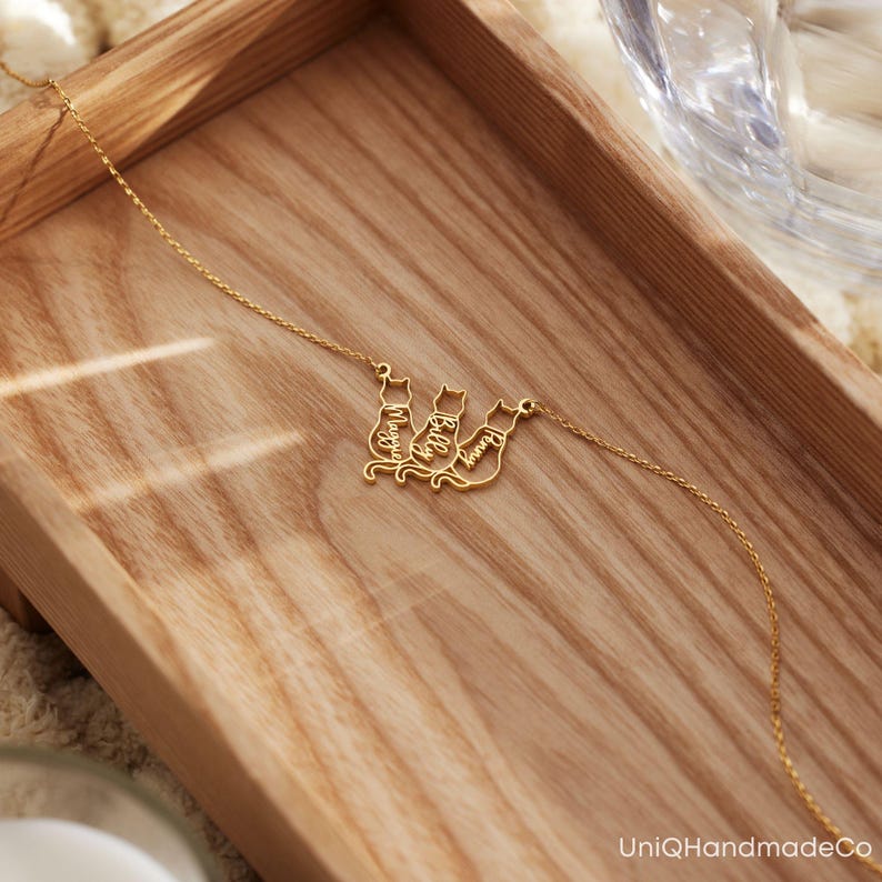 May include: Gold necklace featuring three cat silhouettes, each with a name inscribed: Maggie, Billy, and Sammy.
