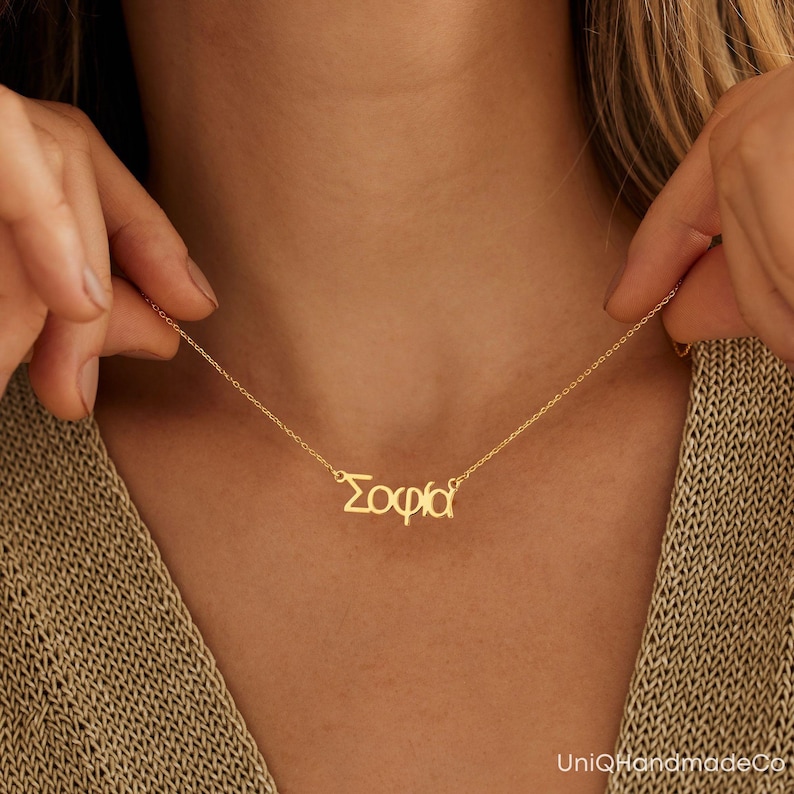 May include: A gold necklace with the name "Sophia" spelled out in Greek letters.