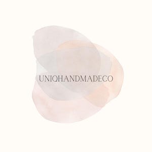 May include: A logo design featuring overlapping watercolor shapes in shades of peach, gray, and off-white. The text "UNIOQHANDMADEDECO" is centered within the design, using a simple, sans-serif font. The background is a soft, off-white color.