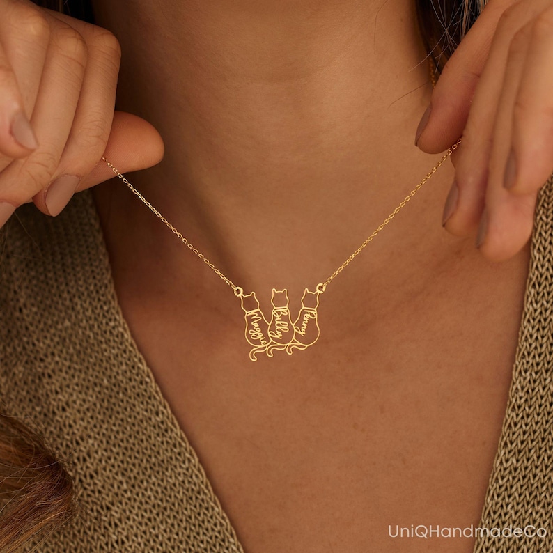 May include: Gold necklace featuring three cat silhouettes, each with a name inscribed: Maggie, Billy, and Penny.