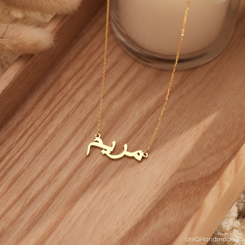 May include: A gold necklace with a delicate chain and a pendant featuring the Arabic word "Salam" in a simple, elegant font.