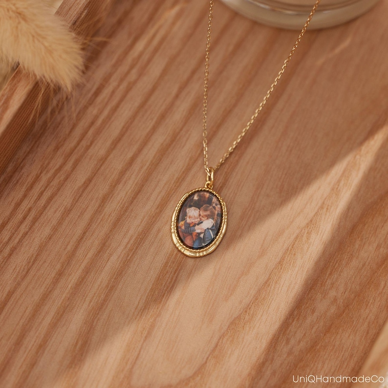 K&ouml;nnte beinhalten: Goldkette mit einem ovalen Anh&auml;nger, der ein Foto von zwei Kindern zeigt, die sich umarmen. Der Anh&auml;nger hat einen goldfarbenen Rahmen.