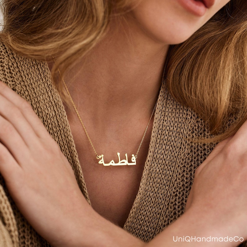 May include: A gold necklace with a nameplate pendant featuring the Arabic word "فاطمة" in a simple, modern font.
