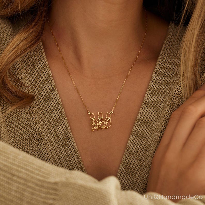 May include: Gold necklace featuring three cat silhouettes, each with a name inscribed inside. The names are "Timmy", "Kelly", and "Maggie".