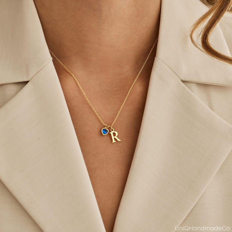 May include: A gold necklace with a blue heart charm and a gold letter 'R' charm.