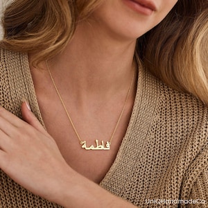 May include: A gold necklace with a nameplate pendant featuring the Arabic word "فاطمة" in a simple, elegant font.