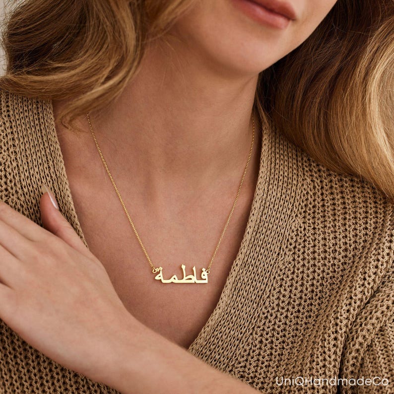 May include: A gold necklace with a nameplate pendant featuring the Arabic word "فاطمة" in a simple, elegant font.