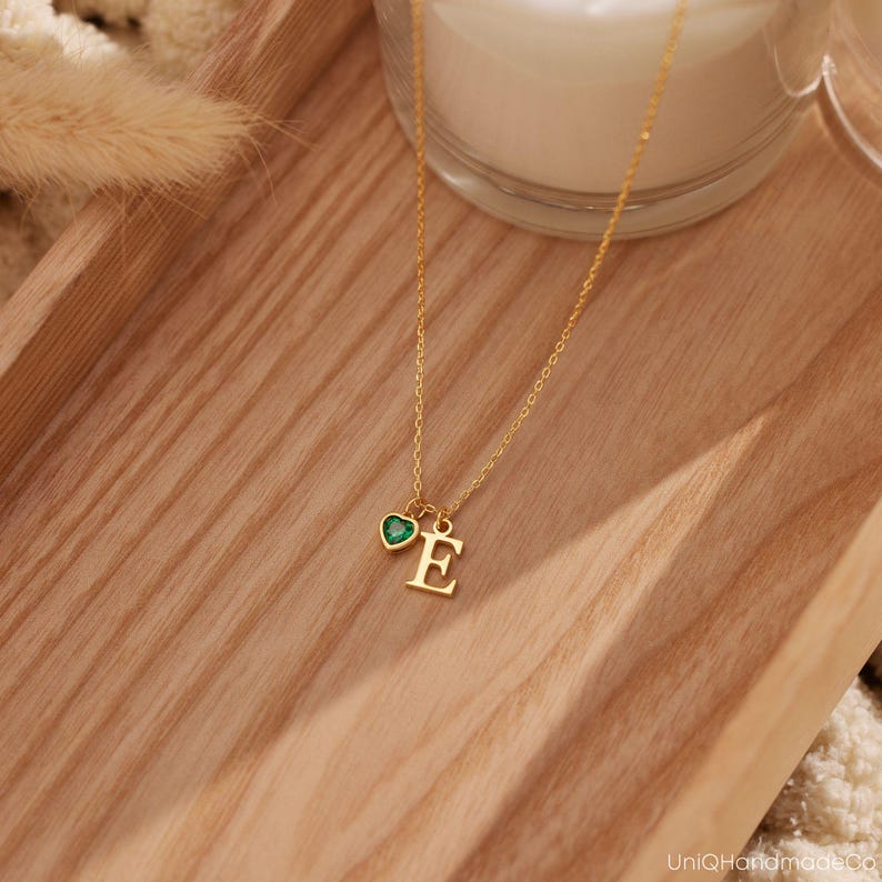 May include: Gold necklace with a small green heart charm and a letter 'E' pendant.