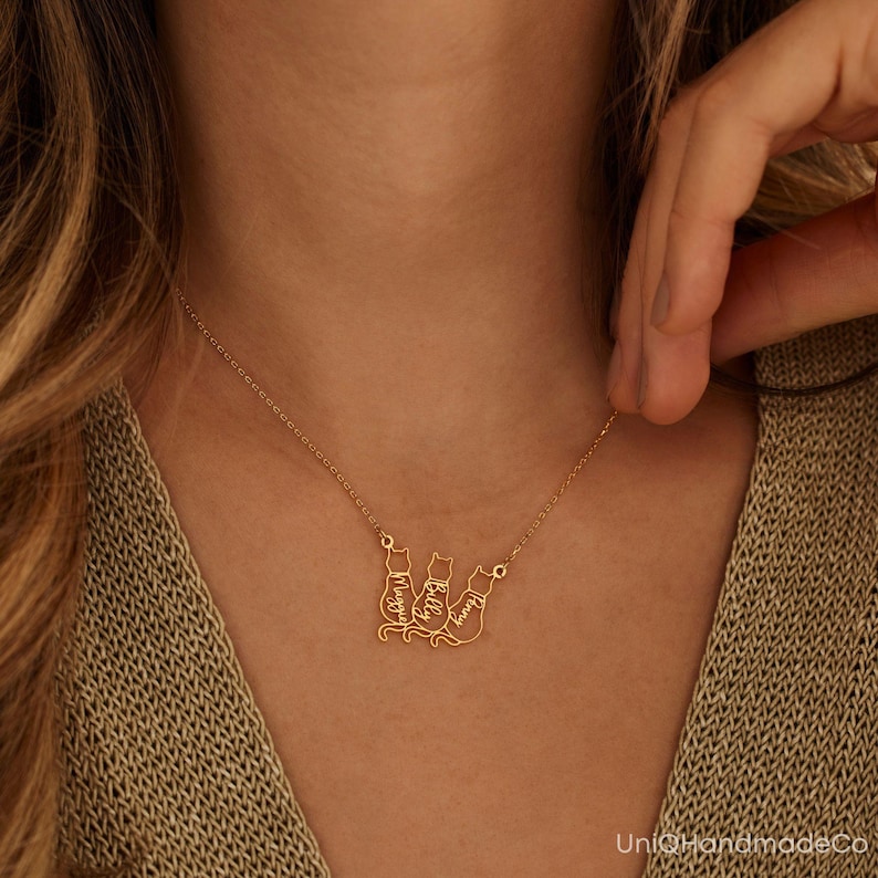 May include: Gold necklace featuring three cat silhouettes, each with a name inscribed inside: Maggie, Billy, and Lucy.