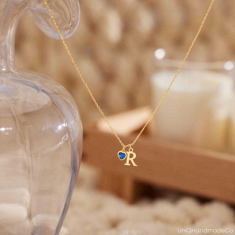 May include: A gold chain necklace with a small blue heart charm and a gold letter 'R' charm.