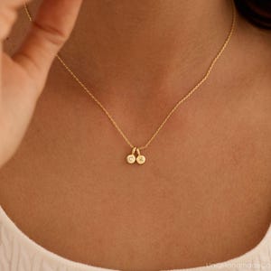 May include: A gold-colored chain necklace featuring two small, circular pendants. Each pendant is engraved with a single letter, one displaying the letter C and the other displaying the letter K. The necklace has a delicate link chain design.