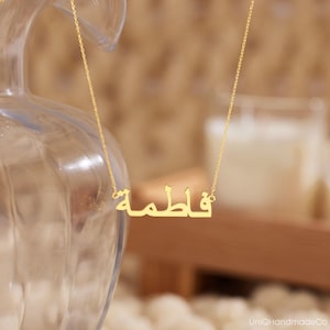 May include: A gold necklace with a nameplate pendant that reads "والطمة" in Arabic script.