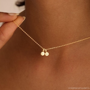 May include: A gold-toned chain necklace featuring two small, circular charms. Each charm is engraved with a single uppercase letter, specifically the letters C and K. The delicate chain connects to the charms, which hang centrally from the necklace.