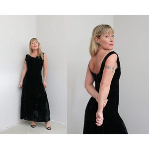 May include: A sleeveless, floor-length black velvet dress. The dress features a scoop neckline and a fitted bodice that flows into a flared skirt. The fabric has a soft, textured appearance. The dress is suitable for formal events.