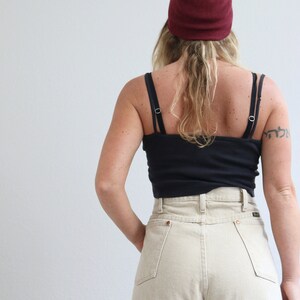 May include: A person wearing a black tank top, beige high-waisted jeans, and a burgundy beanie.