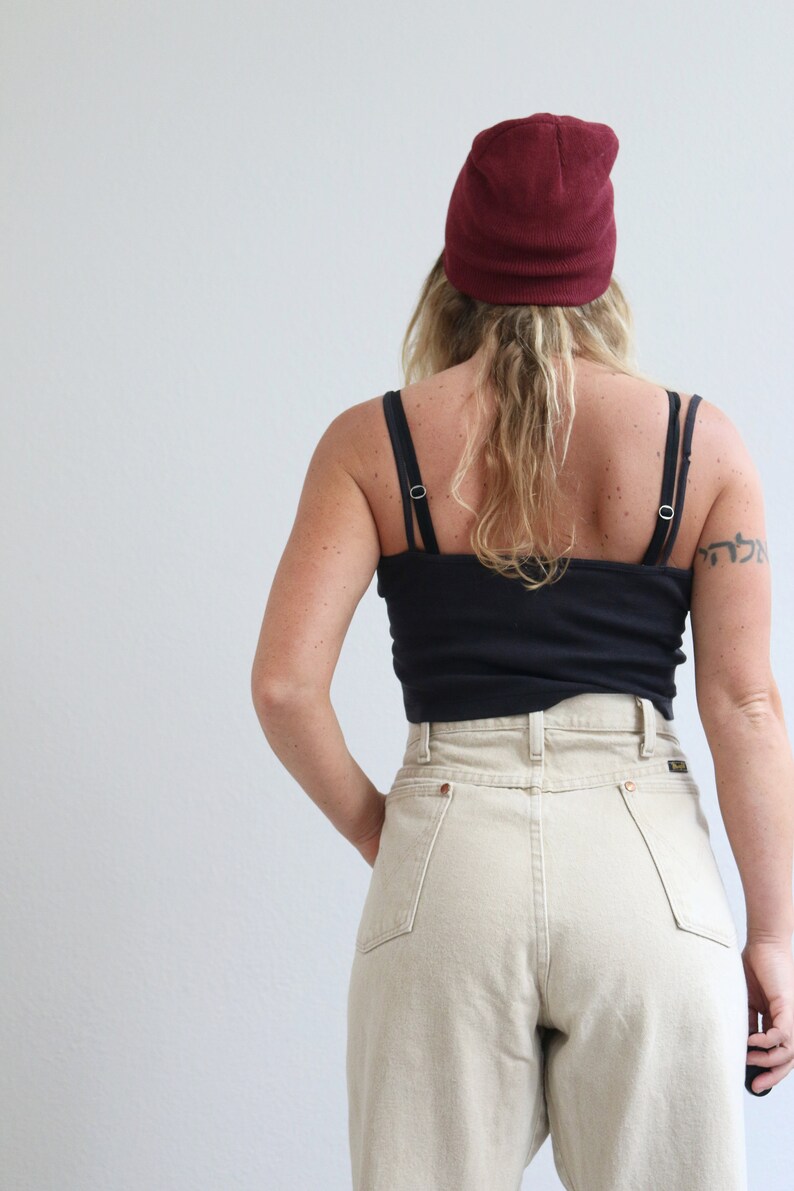 May include: A person wearing a black tank top, beige high-waisted jeans, and a burgundy beanie.